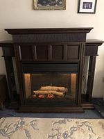 Front view of electric fireplace turned on showing glowing log and flame effect with surrounding glass shelves and wood frame.