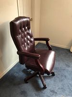 Side angle view of chair showing tufted backrest, wood-finish base and castor wheels