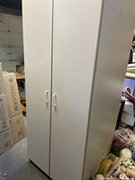 Closed view of the white melamine closet showing 2 doors with handles and the rectangular shape standing on floor.