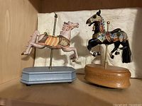 Full view of black and beige carousel horse music boxes on wooden bases showing front and side profiles.