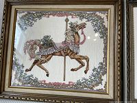 Framed needlepoint of a brown carousel horse with purple flowers in a wooden frame and protective glass.