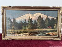 Front view of the framed oil painting showing the full mountainous scene with river and cabin.