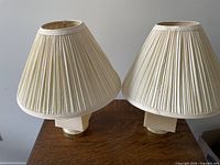 Pair of bedside lamps with cream ribbed fabric shades on table.