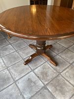 Full view of the round pine table showing the pedestal base and wood grain top on grey tiled floor.