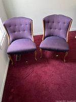 Matched pair of purple traditional style armchairs positioned side by side on a burgundy carpet near a window.