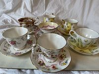 All seven Royal Albert teacups with their matching saucers, arranged on a flat surface showing different floral patterns and colors.
