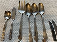 Close-up image of various cutlery pieces showing different types including spoon, knife, fork, and tongs with ornate handles.