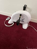 White electric pedal exerciser viewed from the side showing pedals, body and coiled cord remote controller.