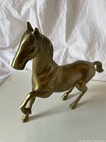 Front-side view of a solid brass horse figurine showing detailed face and raised front leg