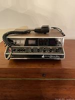 Front view of vintage Cobra 135X mobile CB radio unit with microphone resting on top and front panel showing display and controls.