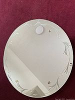 Full view of the round mirror showing the etched leaf pattern around the edges and minor imperfections.