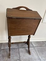 Front view of the vintage wooden standing sewing box showing the double-hinged lid and pedestal stand with turned legs.