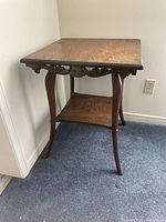 Side view of vintage wooden side table showing carved apron and lower shelf with curved legs.