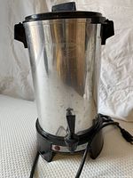 Stainless steel coffee urn with spigot, black base with red indicator, and black handles on sides and lid
