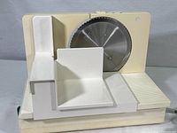 Front view of the Braun home meat slicer showing the beige plastic body, food carriage, and 6-1/2 inch circular cutting blade with scalloped edges.