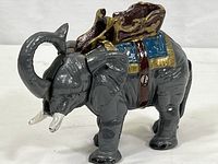 Gray cast iron elephant with blue, gold, and brown painted saddle, tusks, and moving trunk and tail mechanism for coin collection.