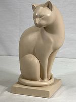 Front view of a warm-white cat cast sculpture showing the main form and posture.