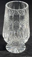 Clear cut crystal pedestal vase showing the full profile, patterned with diamond and vertical cuts, on a dark surface.