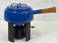 Angle showing full fondue pot mounted on cast iron stand with burner below, blue enamel body and teak wood handle