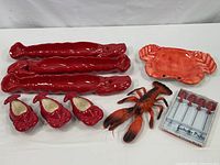 Full lot showing three long red lobster-shaped ceramic serving servers, matching lobster butter dishes, a plastic lobster decor, and four boxed lobster picks.