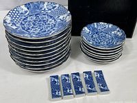 Stack of ten large 6-1/2 plates, seven smaller 4-3/4 plates, and five chopstick rests in front with a wooden storage box behind them