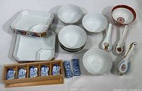 Photo displaying seven mismatched porcelain bowls, two divided plates, a box of ceramic chopstick rests, and four ceramic spoons decorated with traditional Chinese patterns.