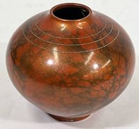 Photo of a round-bodied enameled brass vase with rosy bronze coloration and subtle darker branch-like design, showing circular etched rings near the neck opening.