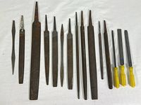 Full collection of 17 metal files arranged on white cloth, showing variety of file shapes and handle types including wooden and yellow plastic handles.