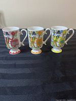 Front view of three Royal Crown Arnart ceramic mugs with colorful character art and balloons in bright reds, yellows, oranges on pedestal bases