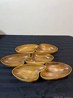 Front view showing six wooden bowls/dishes placed in a cluster on a black surface. Bowls are medium brown with smooth finish.