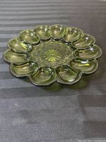 Top view of the avocado green glass egg plate showing the twelve egg compartments and decorative starburst pattern in the center.