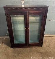 Front view of a dark wood barrister-style display cabinet featuring glass front doors and brass knobs, light blue fabric interior visible through glass.