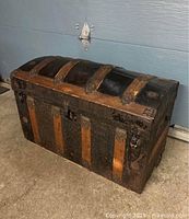 Full view of antique humpback steamer trunk showing curved top, wood slats and metal accents.