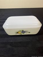 Butter dish with lid showing fruit design on side, white glass base, rectangular shape.