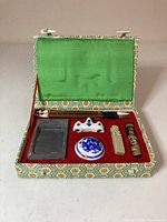 View of Chinese calligraphy set in an open patterned fabric box showing all included tools arranged on red felt.