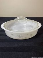 Full view of white Glasbake Starburst round casserole dish with clear glass lid on black surface.