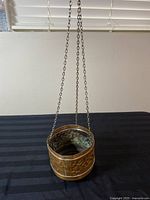 Copper hanging planter displayed on a black surface with chains extended, showing hanging mechanism and overall dimensions.