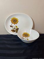Oval sunflower-printed platter and matching serving bowl on black fabric background.