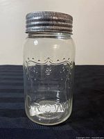 Clear glass mason jar showing embossed 'CROWN' and crown emblem on the front with metal screw lid.