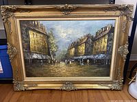 Full view of the framed oil painting depicting a street scene with figures and buildings under a cloudy sky.