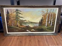 Full view of the ornate gold-framed landscape painting depicting a mountain lake scene with birch and evergreen trees.