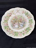 Full view of the decorated scalloped edge plate featuring floral border and central illustration of two mice in a cottage setting.