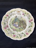 Full view of one collector plate titled 'The Plan' featuring Jill Barklem illustration with floral border and scalloped edge.