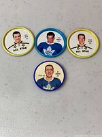 Top-down view of four round hockey tokens featuring NHL players. One blue plastic token with Al Arbour, three metal Sheriff tokens with All Star players.