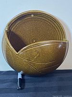 Front view of the glazed pottery wall decor showing the leaf relief design and curved opening for shelf or pocket use.