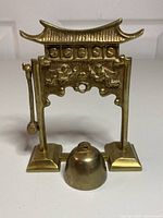 Front view of solid brass hanging bell with mallet removed, showing intricate design and detached bell.