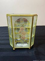Front side of the vintage brass miniature curio display cabinet showing beveled glass with oval floral etching and interior shelves.