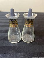 Pair of vintage Mid-Century Modern style glass salt and pepper shakers showing front and side views, with black stopper tops and gold banding around upper glass section.