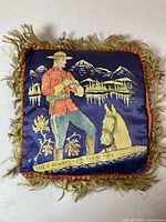 Front view of the vintage RCMP pillow showing officer, horse, mountains, and phrase 'THEY ALWAYS GET THEIR MAN' with fringed edges.