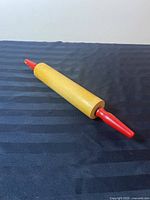 Full view of vintage wooden rolling pin with red handles placed on a black fabric background, showing slight wear on the red paint of the handles.